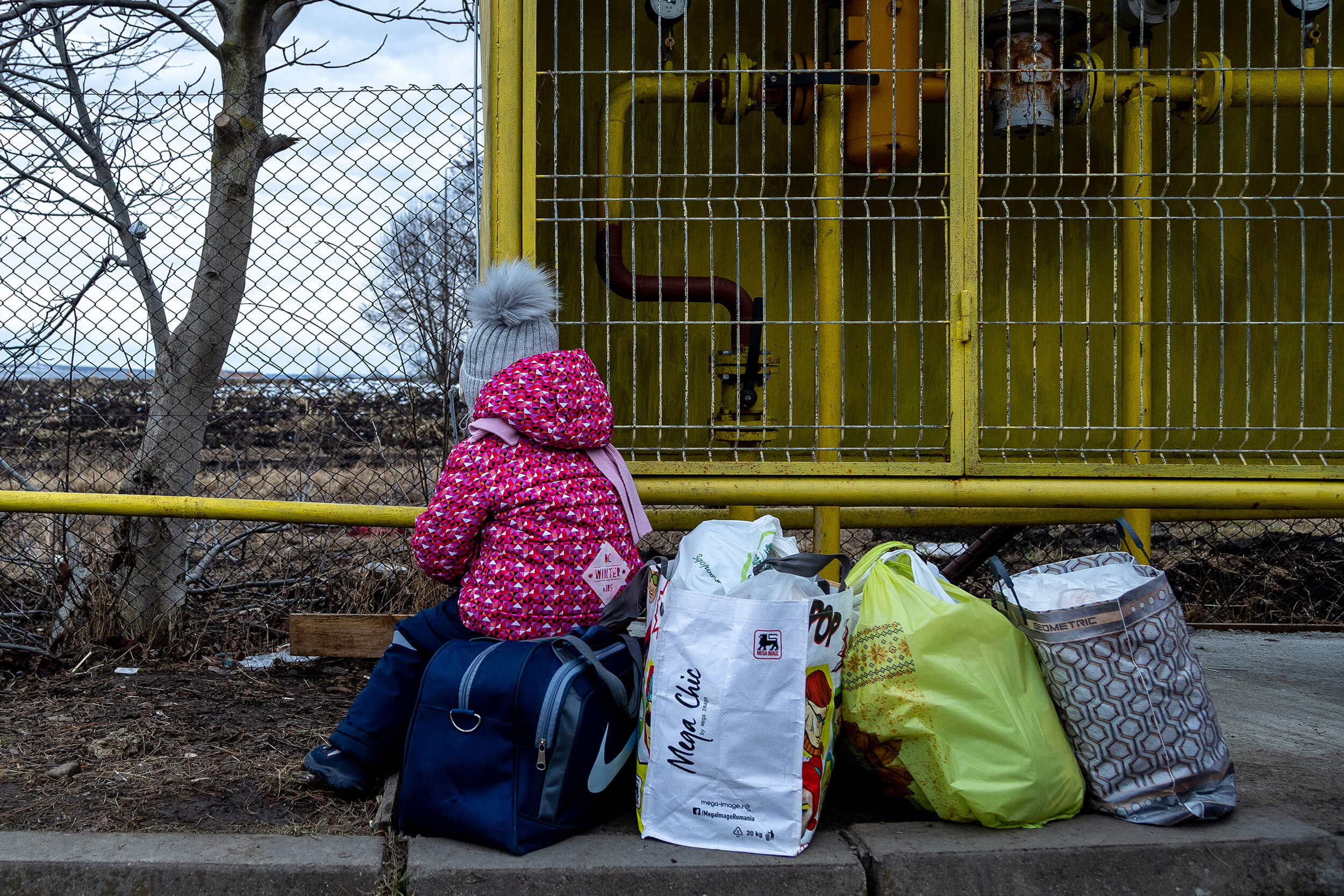 A two-year-old girl sits on her family’s luggage while waiting for a van that will take them to buses waiting to take them to other cities in Romania or to different countries across Europe.