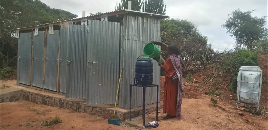 Radia adds water to the handwashing station as she cleans the new latrine.