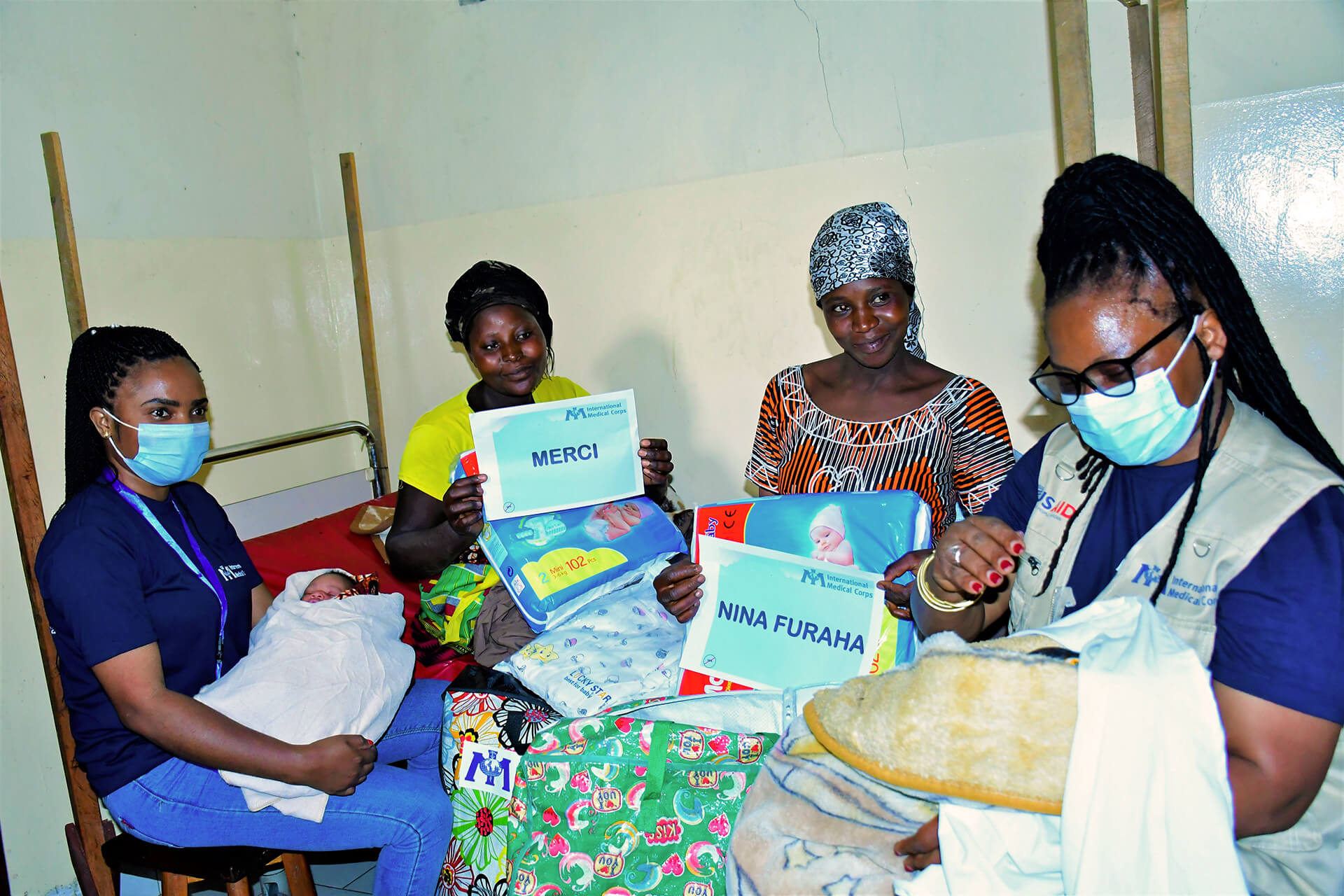 Asha Kisitu (far left) and Yvonne Uwimana (far right) cradle the babies of women displaced by the Nyiragongo volcano eruption after handing out maternity kits.
