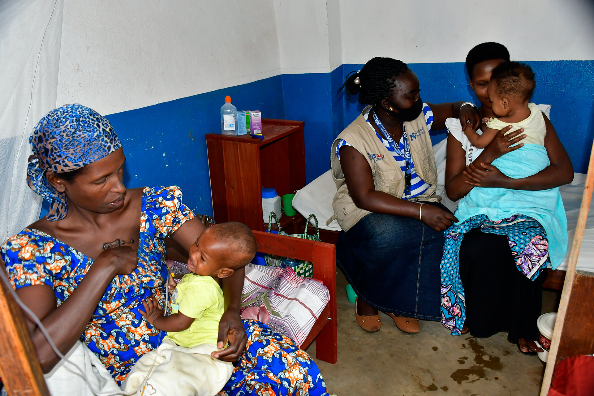 Nyamasoso Dyna (at left), an IDP in Uvira, holds her child while International Medical Corps staff member Melissa visits another mother to monitor the quality of care provided to war-displaced people.