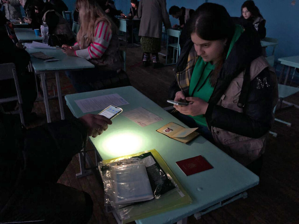 Despite frequent power outages, staff members continue to register people—even if it requires working under light provided by mobile phones.