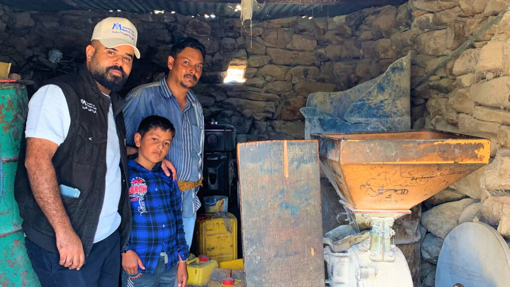 Nasir stands in his mill with his son Mohammed and International Medical Corps Food Security and Livelihoods Assistant Hussam Mahfoudh.