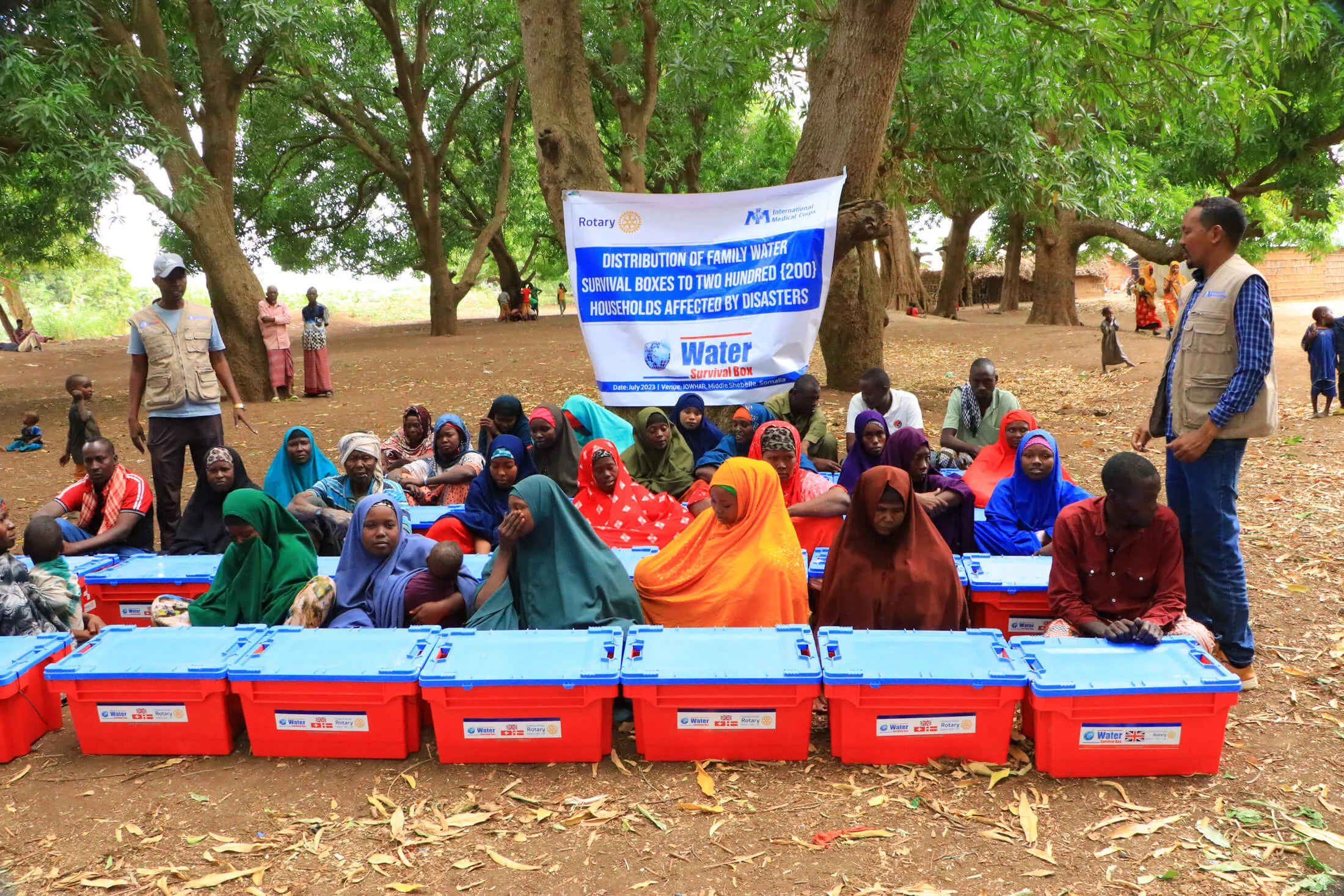 Staff members demonstrate how the water purifier works as families listen and receive their water survival boxes.