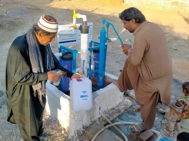 Community members collect water from a hand pump.