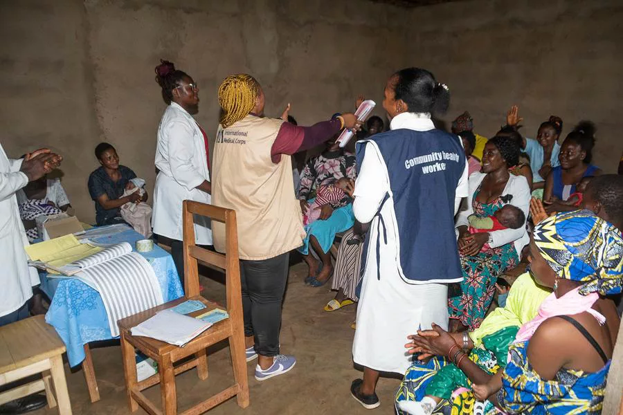 Marion Ayuk (tan vest), Program Assistant, and Bertha Tabi (white lab coat) and Banaki Grace (dark blue apron), volunteer midwives, educate mothers about childhood illnesses. Our teams conduct these educational sessions while community members await no-cost health consultations at our Fonfuka health outpost’s infant welfare clinic.