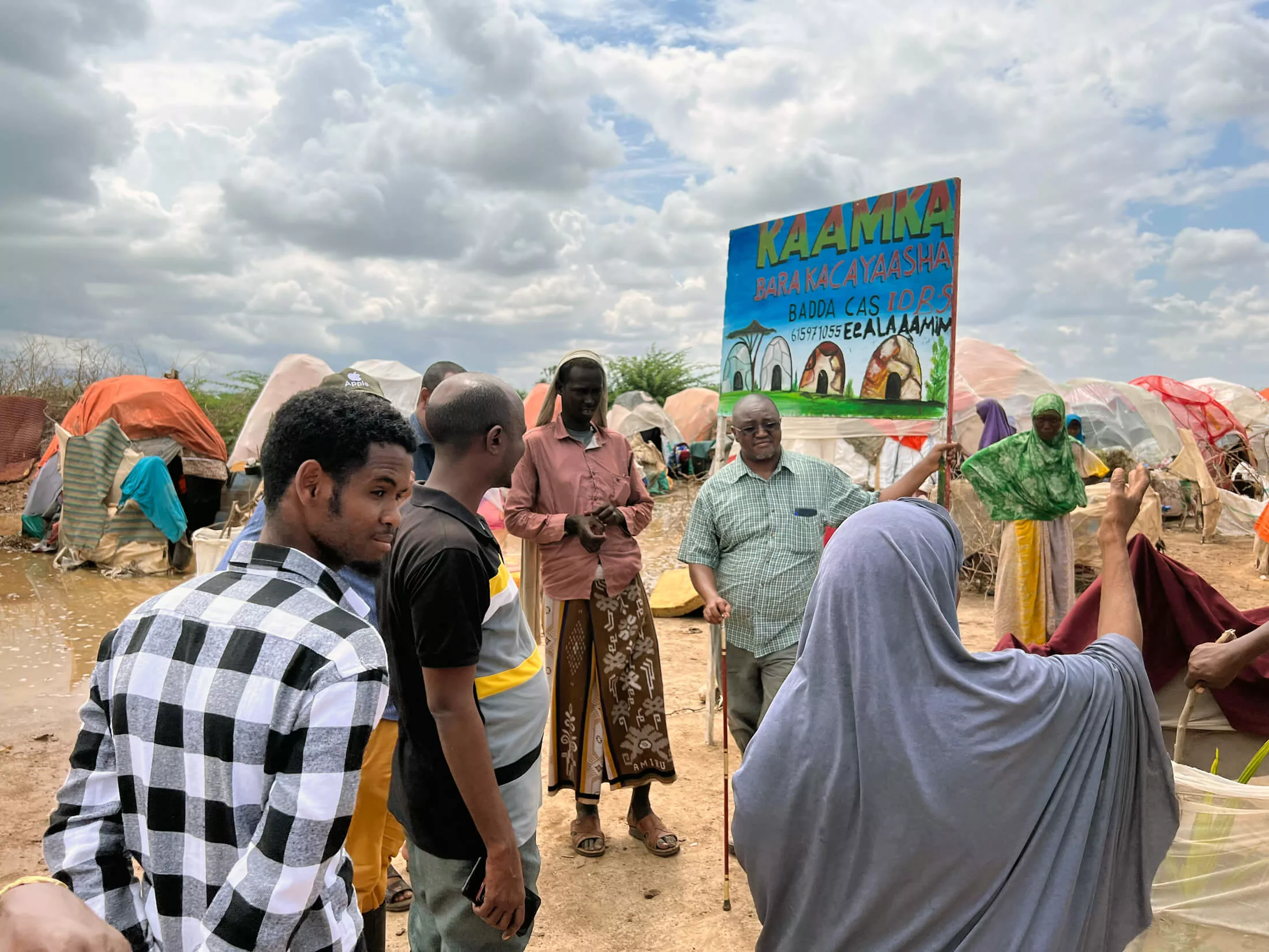 Njoroge Kamau (wearing green, beneath sign) assesses the needs at Badacaas camp for internally displaced persons in Jowhar, Somalia.