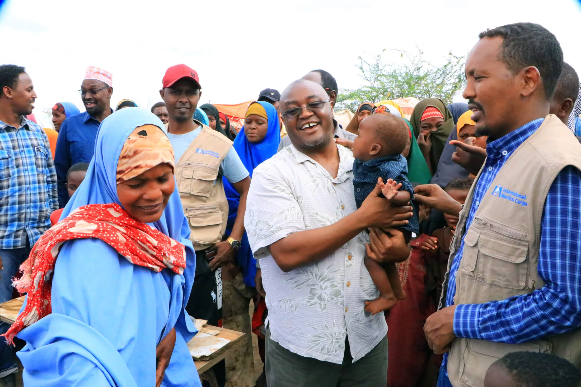 Njoroge Kamau holds a baby, while surrounded by International Medical Corps staff and beneficiaries.