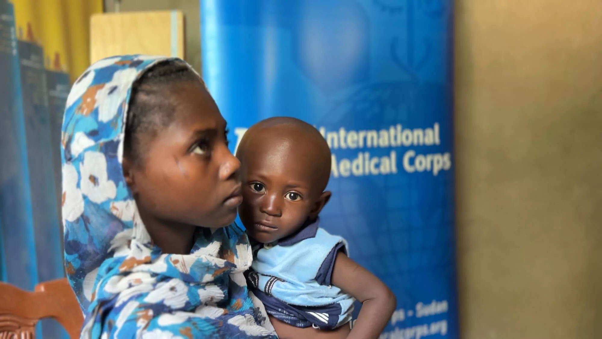 Radia Osman, 13, holds her brother, Musab, waiting for Namariq to take his MUAC measurement. Radia accompanied her mother and siblings to the clinic.