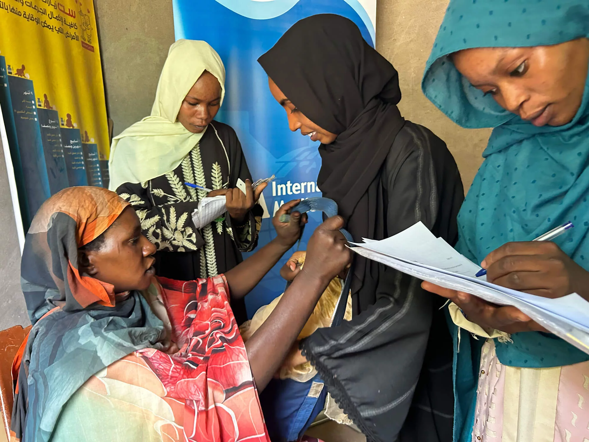 Namariq Elhadi Nasir takes Habooba’s height and weight measurements to determine if she is malnourished, while Safa Jaafar Abdul Kareem and Nidaa Muhktar Billo Osman—who are Therapeutic Nutrition Officers with International Medical Corps—fill out paperwork and bring supplies.