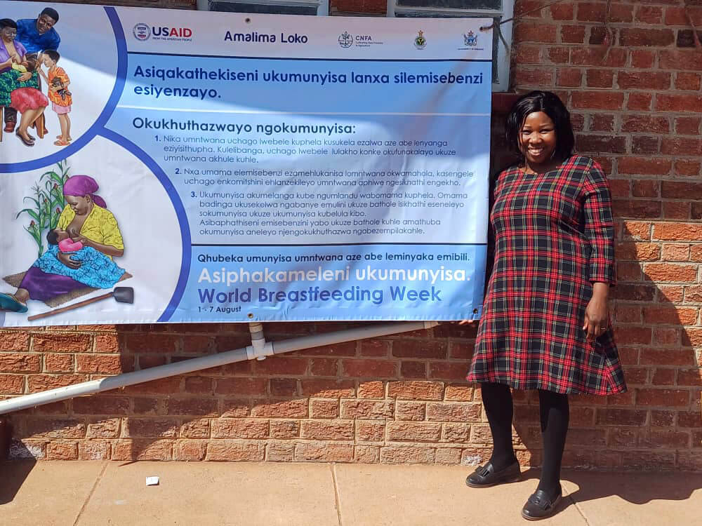 Murakwani poses in front of a sign promoting World Breastfeeding Week.